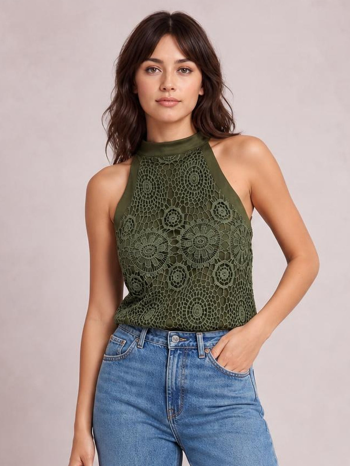 A model wears an olive-green lace mock neck tank with a sleeveless high-neck silhouette and straight hem, posing with one hand in her jeans pocket.