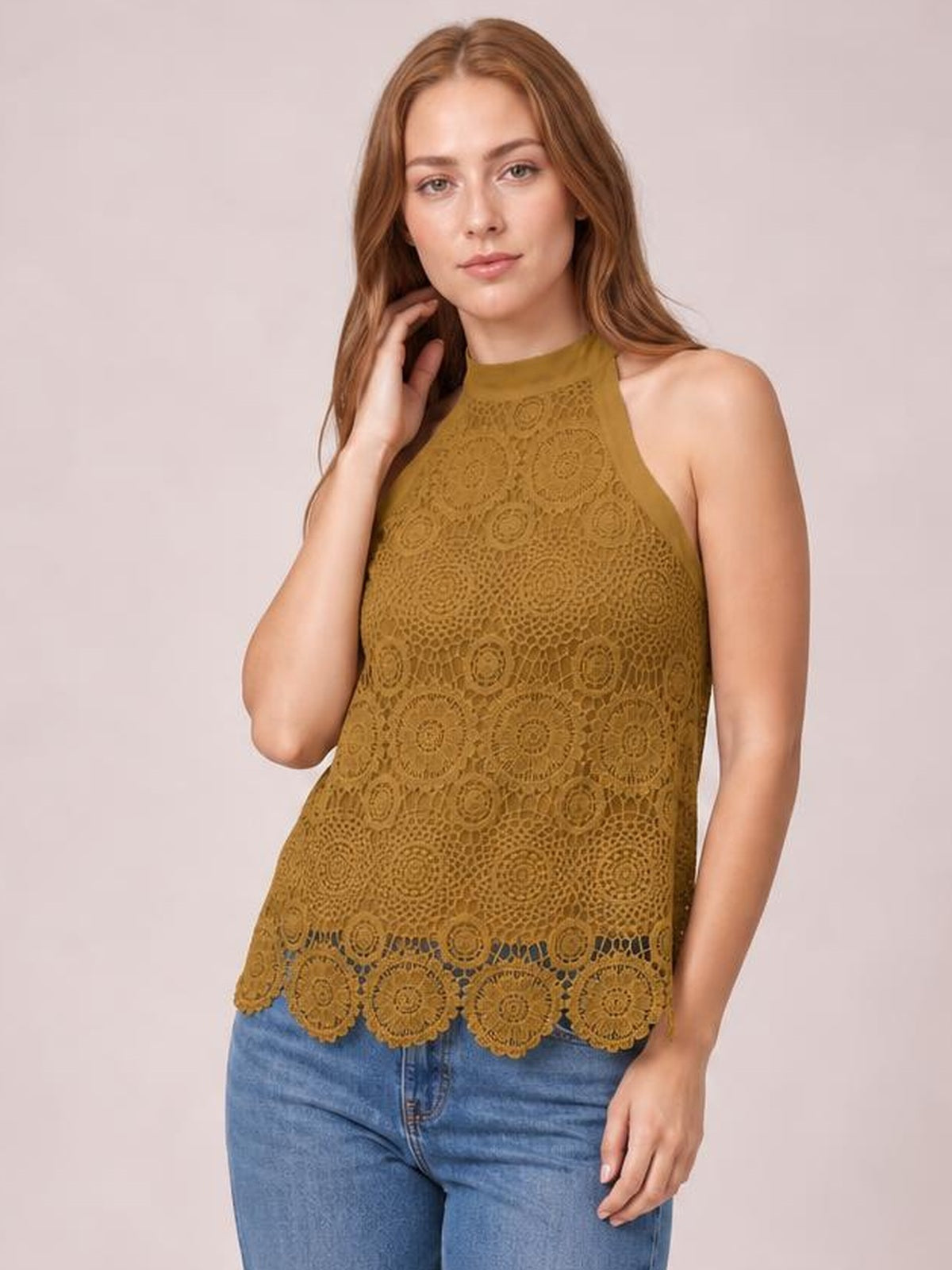 Model poses with one hand near her hair in a mustard lace mock-neck tank featuring a sleeveless silhouette, relaxed fit, and scalloped hem.