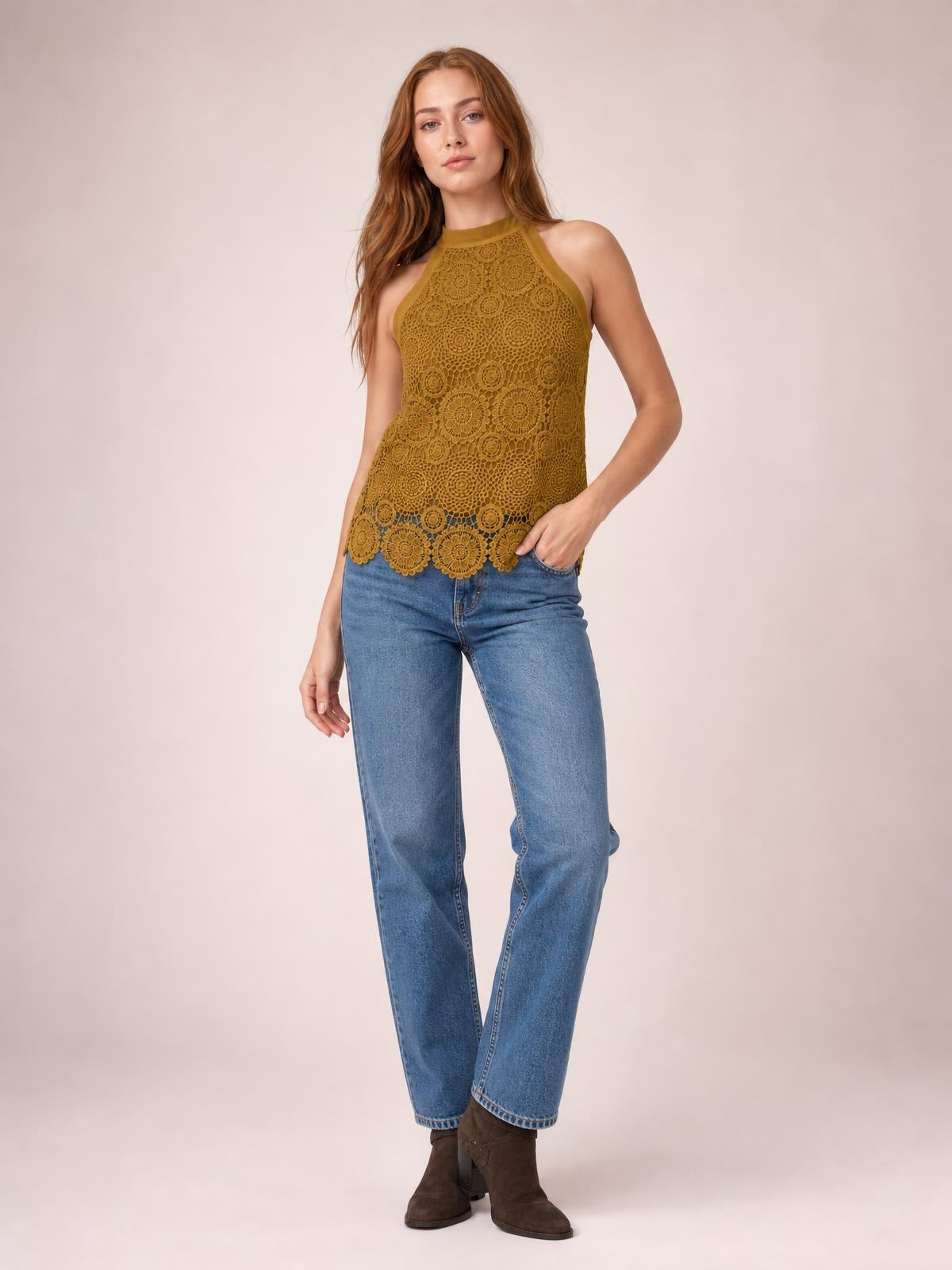 Model poses in a mustard lace mock neck tank with a fitted sleeveless silhouette and scalloped hem, paired with jeans.