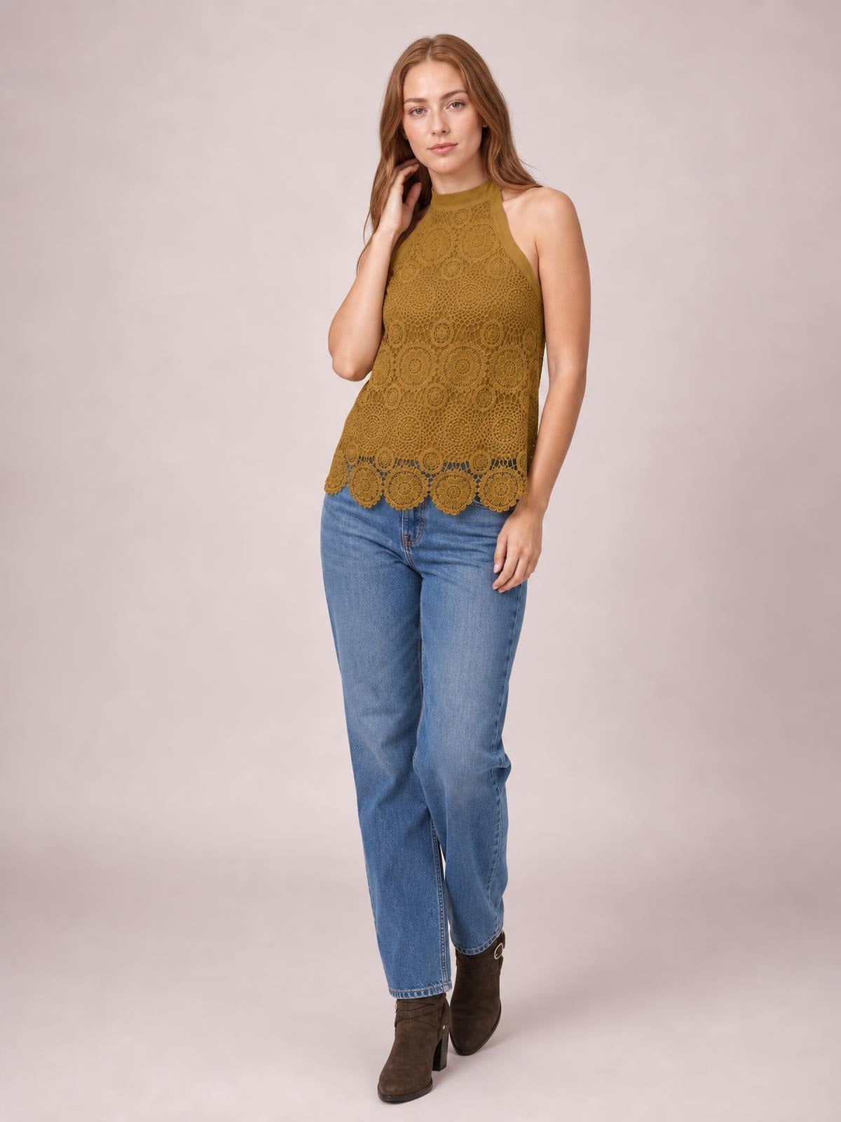 Model poses with one hand near her neck in a mustard lace tied mock neck tank featuring a straight silhouette and scalloped hem.