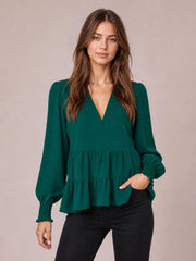 Model poses in a deep green blouse with a notched neckline, voluminous lantern sleeves, ruched cuffs, and a tiered peplum silhouette.