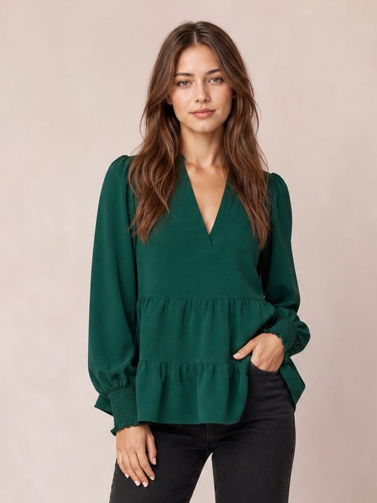 Model wears a deep green notched-neck blouse with ruched lantern sleeves, smocked cuffs, and a tiered, relaxed peplum silhouette.