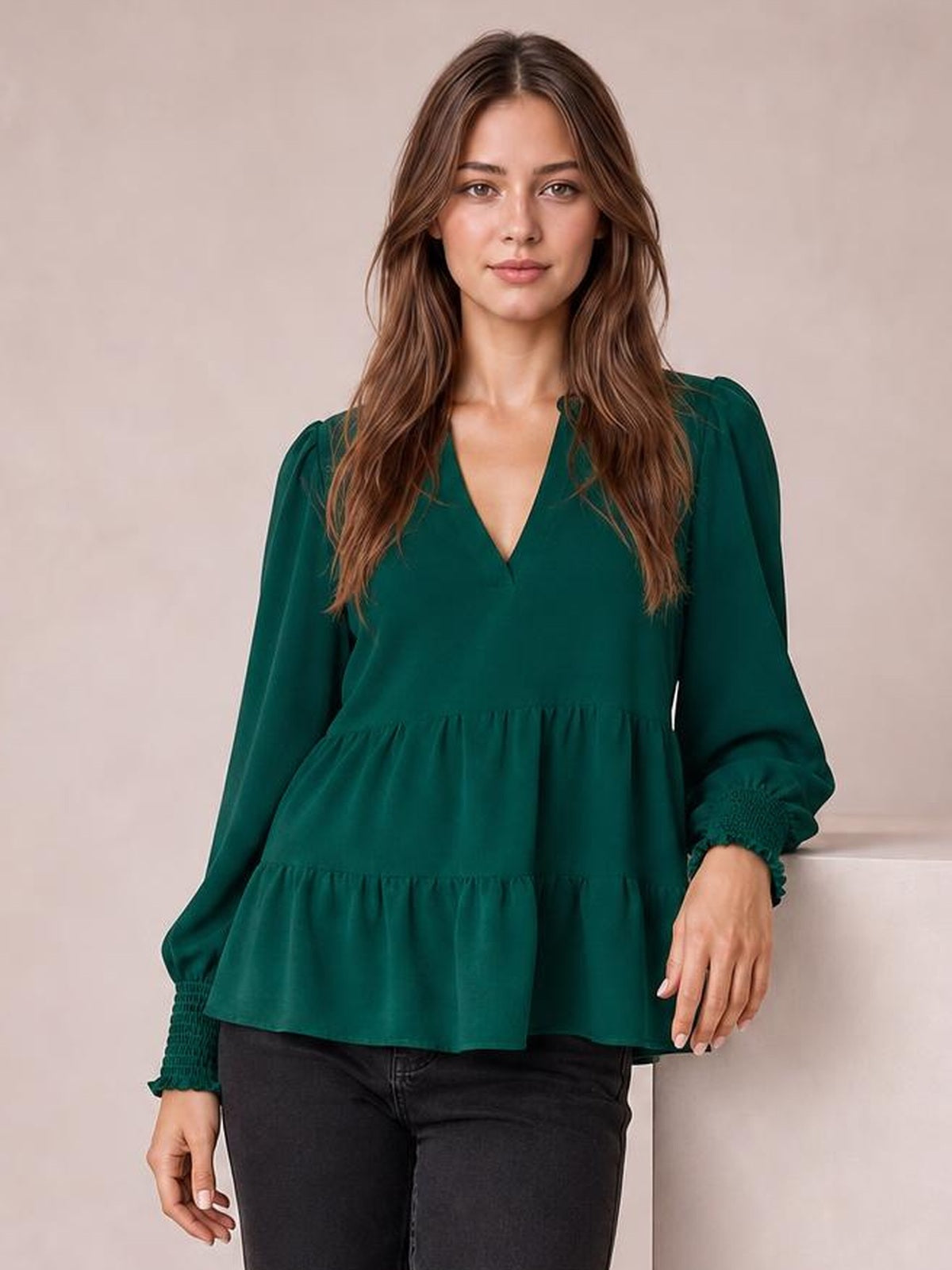 A model wears a deep green notched-neck blouse with voluminous lantern sleeves, ruched cuffs, and a gathered tiered peplum silhouette.