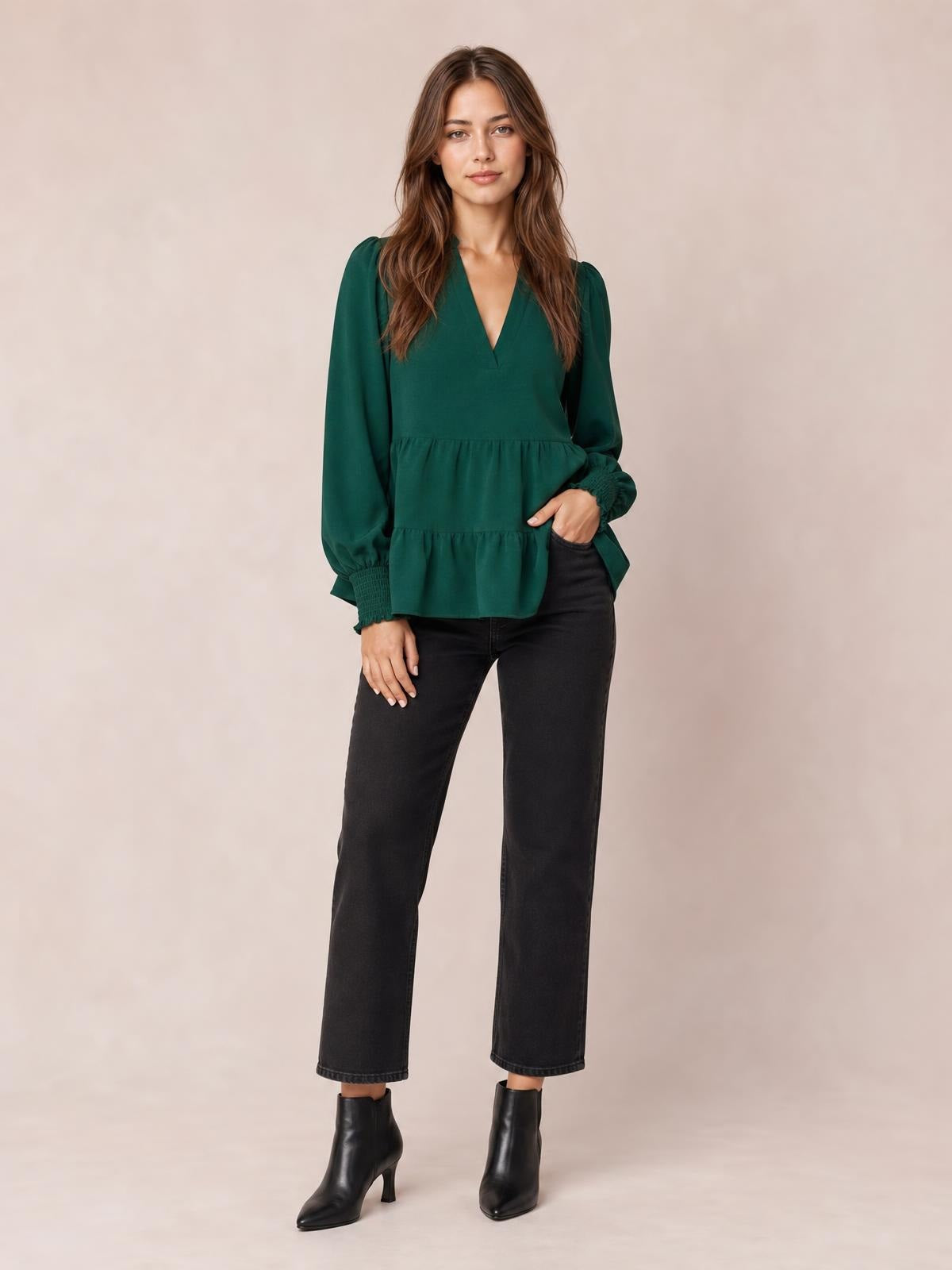 A model stands in a dark green notched-neck blouse with voluminous lantern sleeves, ruched cuffs, and a softly gathered tiered silhouette.