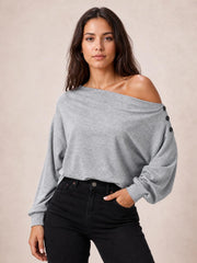 Model wears a solid gray off-shoulder long sleeve blouse with a relaxed silhouette, regular length, and button detailing along the shoulder.