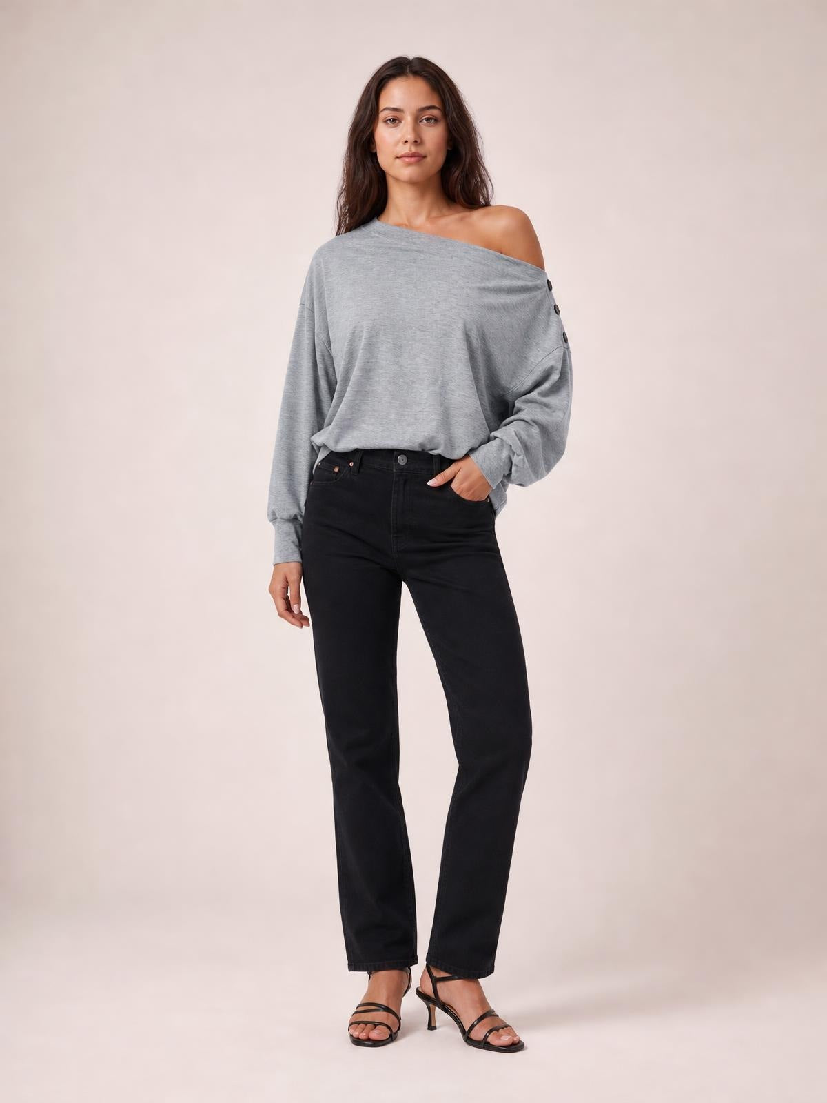 Model wearing a solid gray off-shoulder blouse with long regular sleeves, relaxed silhouette, and button detailing along the shoulder, standing with one hand in her pocket.