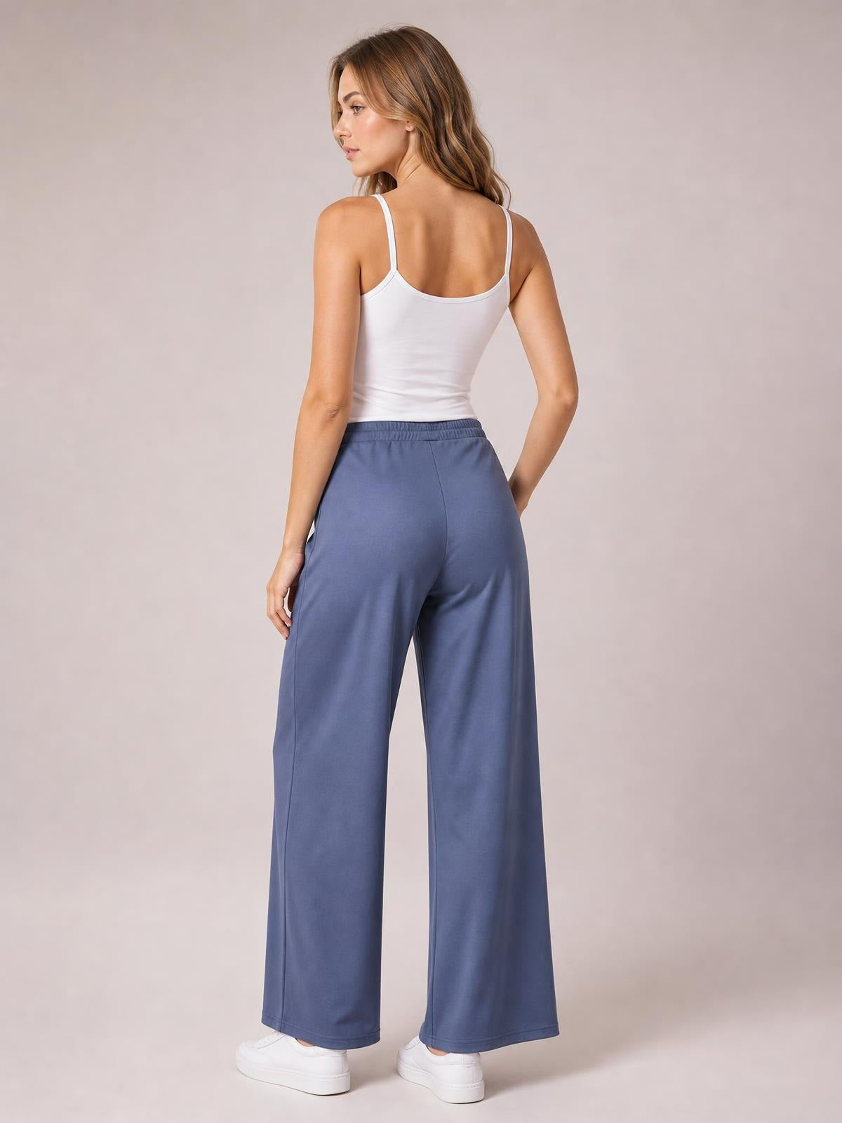 Model poses turned away in blue solid pleated-detail wide-leg pants with an elastic waistband, side pockets, and a long relaxed silhouette.