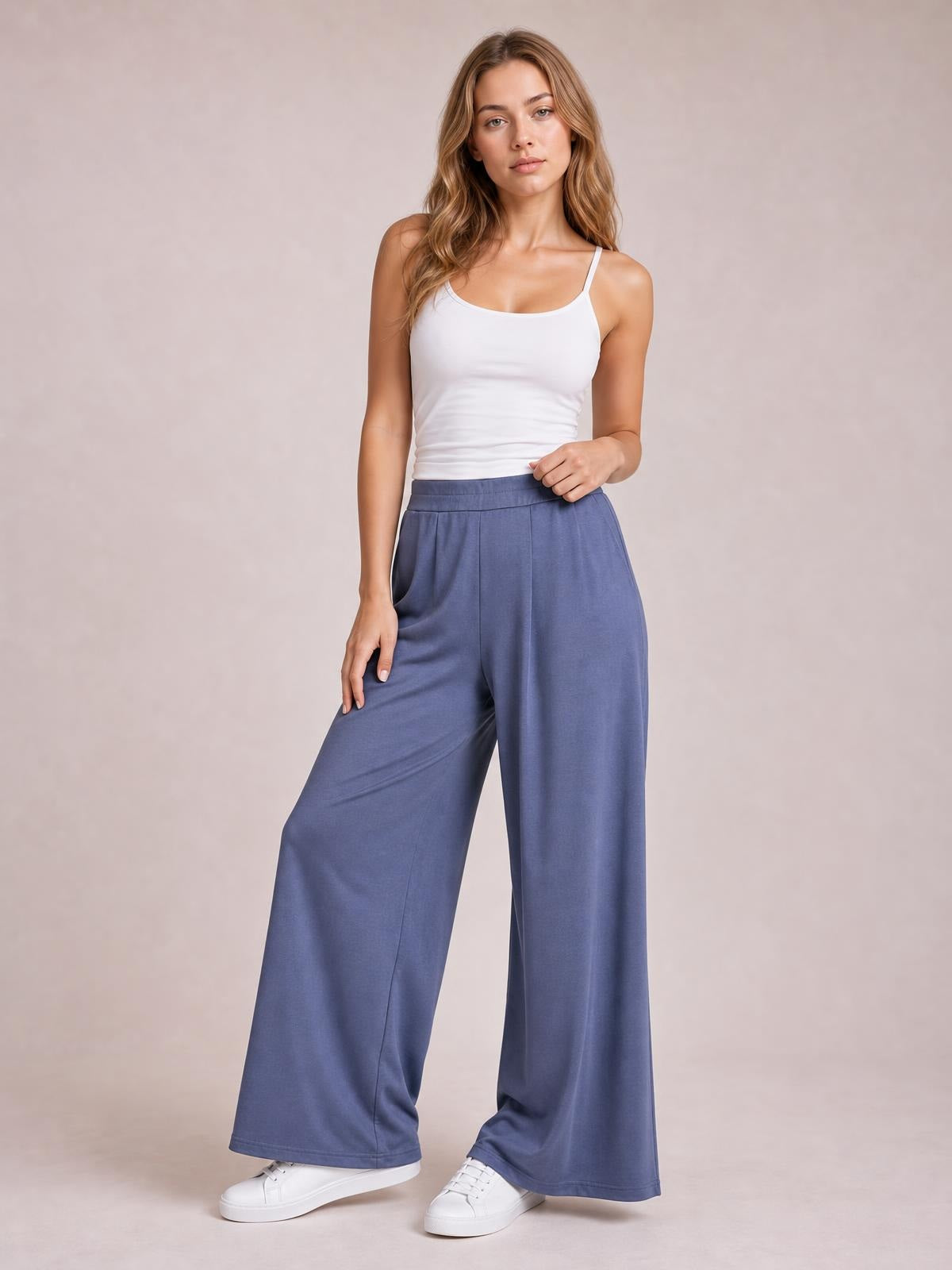 A model poses in dusty blue pleated detail wide-leg pants with a high waistband, side pockets, long flowing legs, and a relaxed casual silhouette.