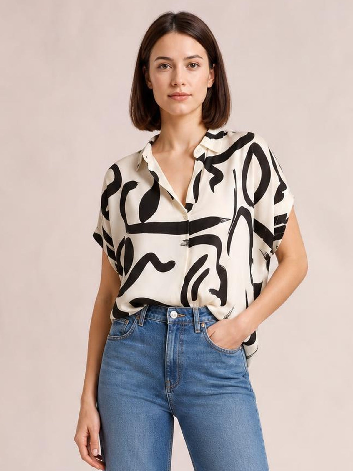Model wearing an opaque cream printed blouse with bold black abstract patterns, a notched neckline, short sleeves, and a relaxed straight silhouette.