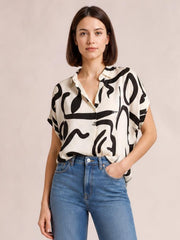 Model wearing an opaque cream printed blouse with bold black abstract patterns, a notched neckline, short sleeves, and a relaxed straight silhouette.