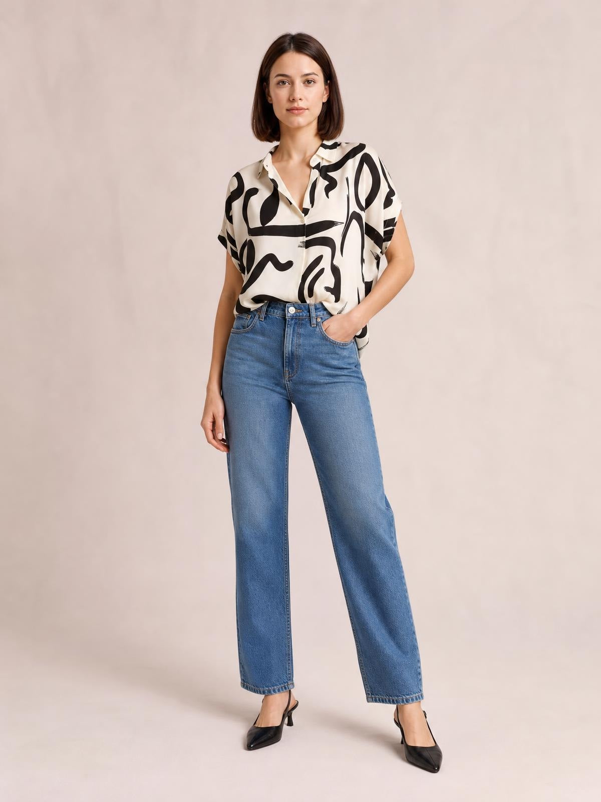 A model wears a cream-and-black printed notched half sleeve blouse with a relaxed silhouette and button-front construction, posing with one hand in her jeans pocket.