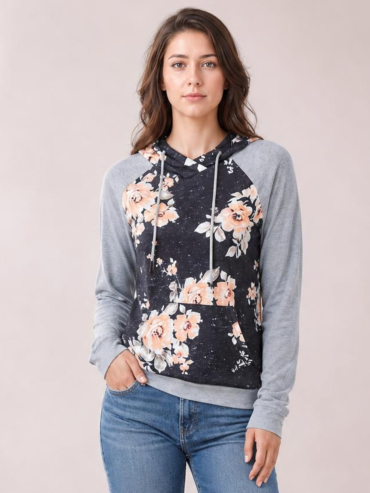 Model wears a black floral printed raglan sleeve hoodie with gray long sleeves, drawstring hood, kangaroo pocket, and regular silhouette, standing with one hand tucked inside.