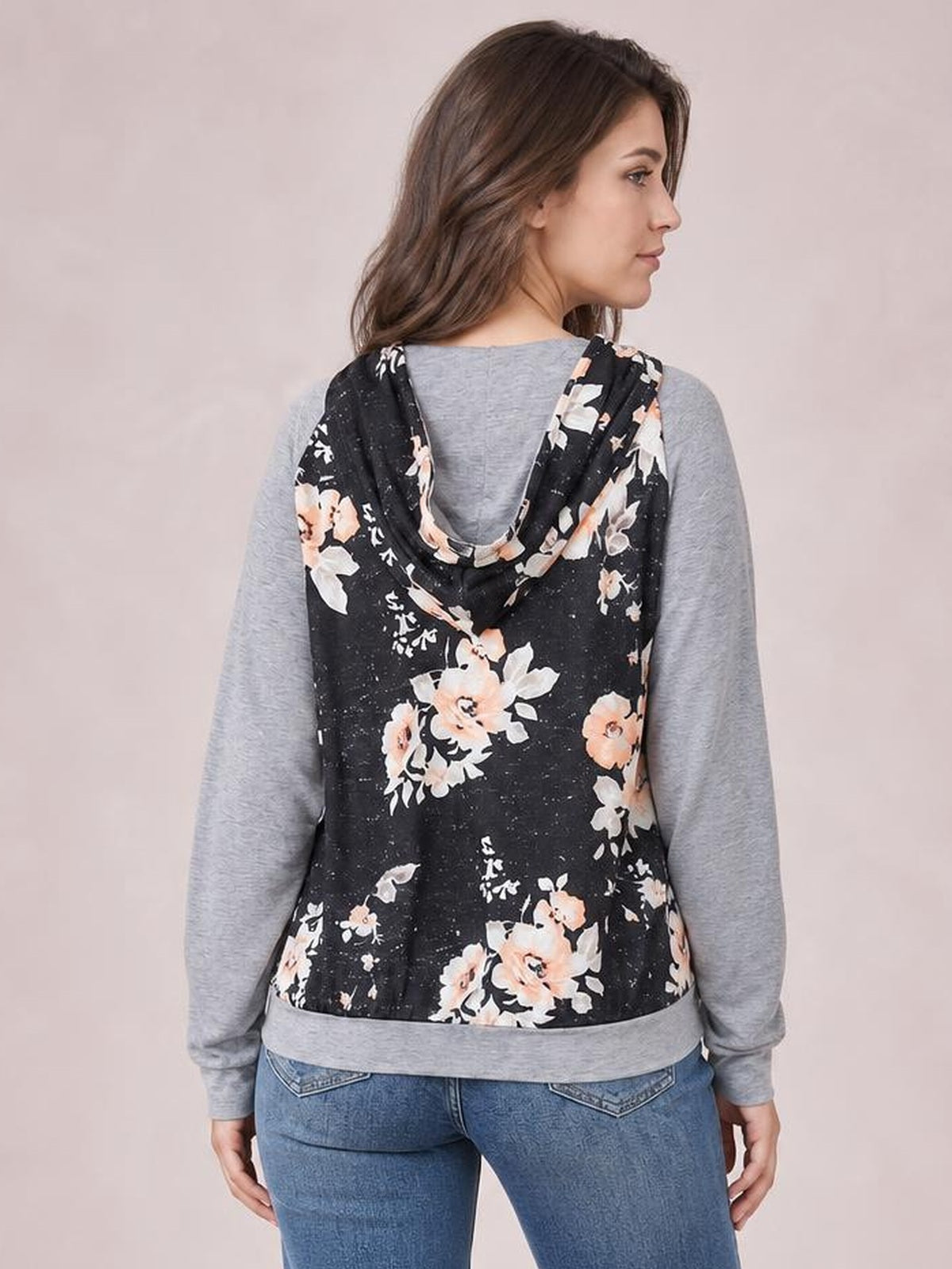 A model stands turned away in a regular-length black floral hoodie with a draped hood, gray long raglan sleeves, and a relaxed casual silhouette.