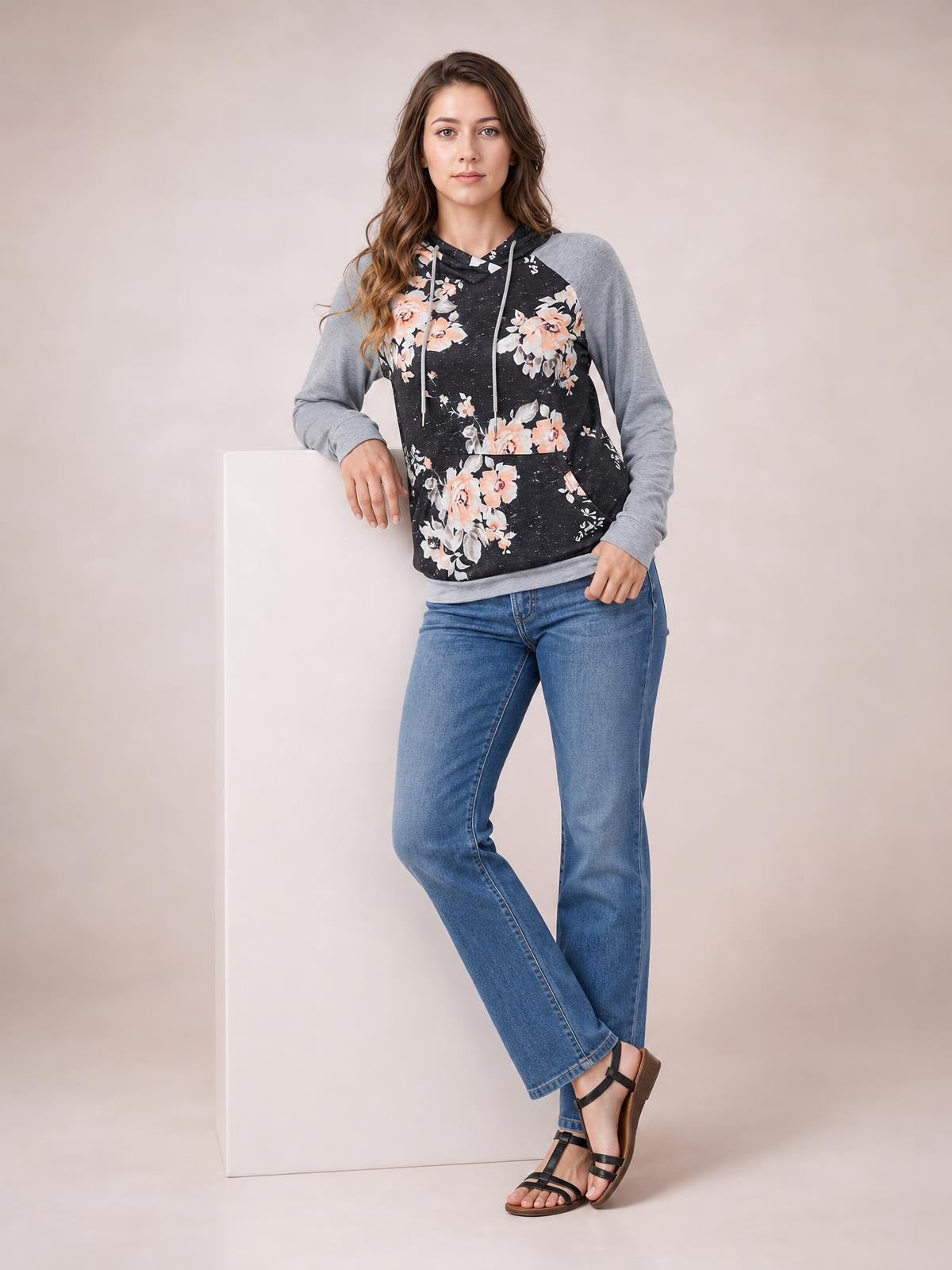Model wearing a casual floral printed raglan sleeve hoodie with a black body, gray long sleeves, hood, drawstring, front pocket, and regular-length silhouette.
