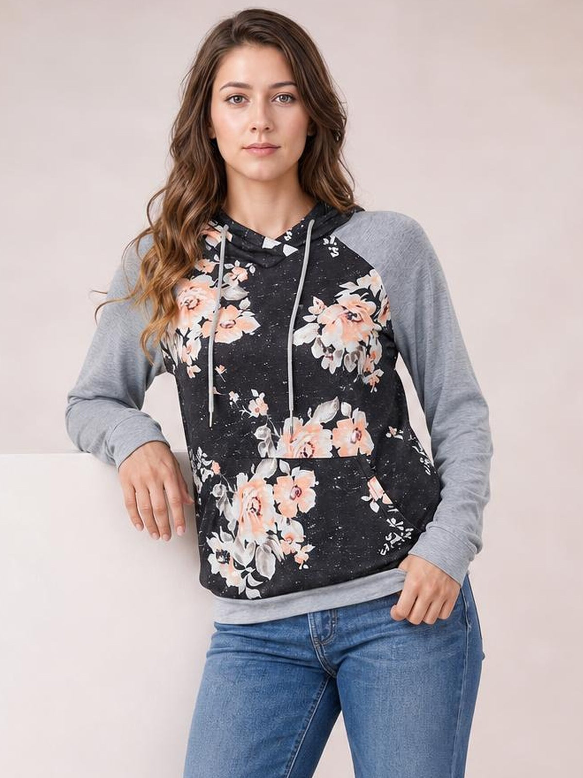 Model poses in a black floral printed raglan sleeve hoodie with gray long sleeves, drawstring hood, kangaroo pocket, and regular-length silhouette.