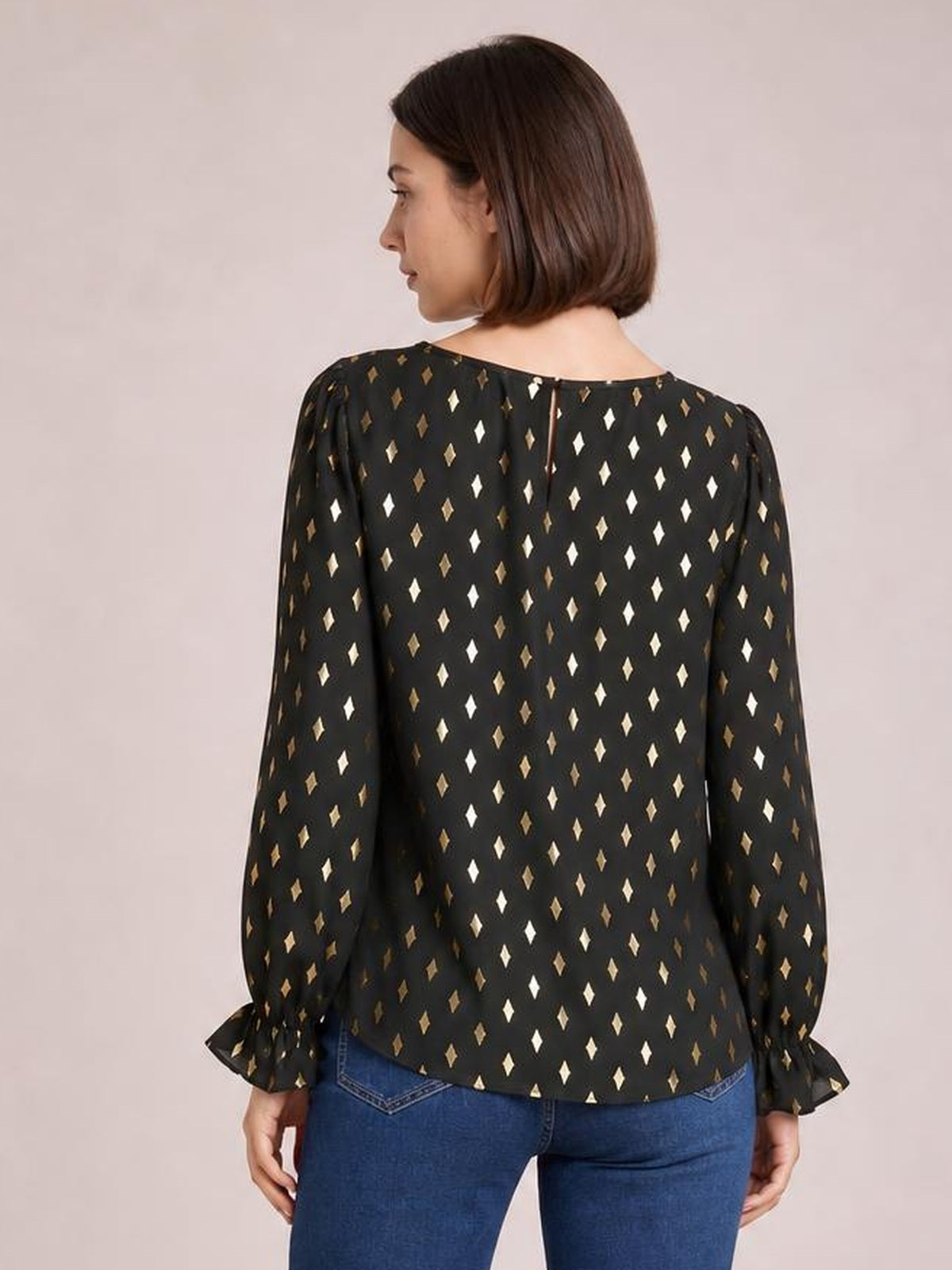Model shown from behind wearing a black printed blouse with a round neckline, long puff sleeves, flounce cuffs, and a relaxed long silhouette.