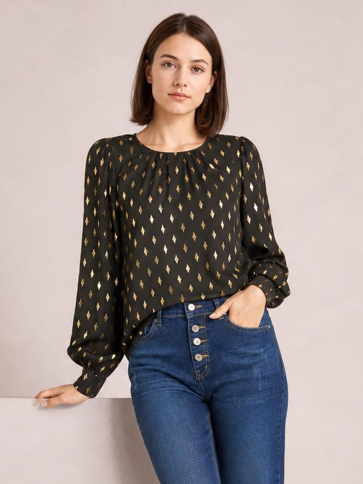 Model wearing a black printed blouse with a round neck, gathered detail, long puff sleeves, and a relaxed silhouette, posing with one hand in her jeans pocket.