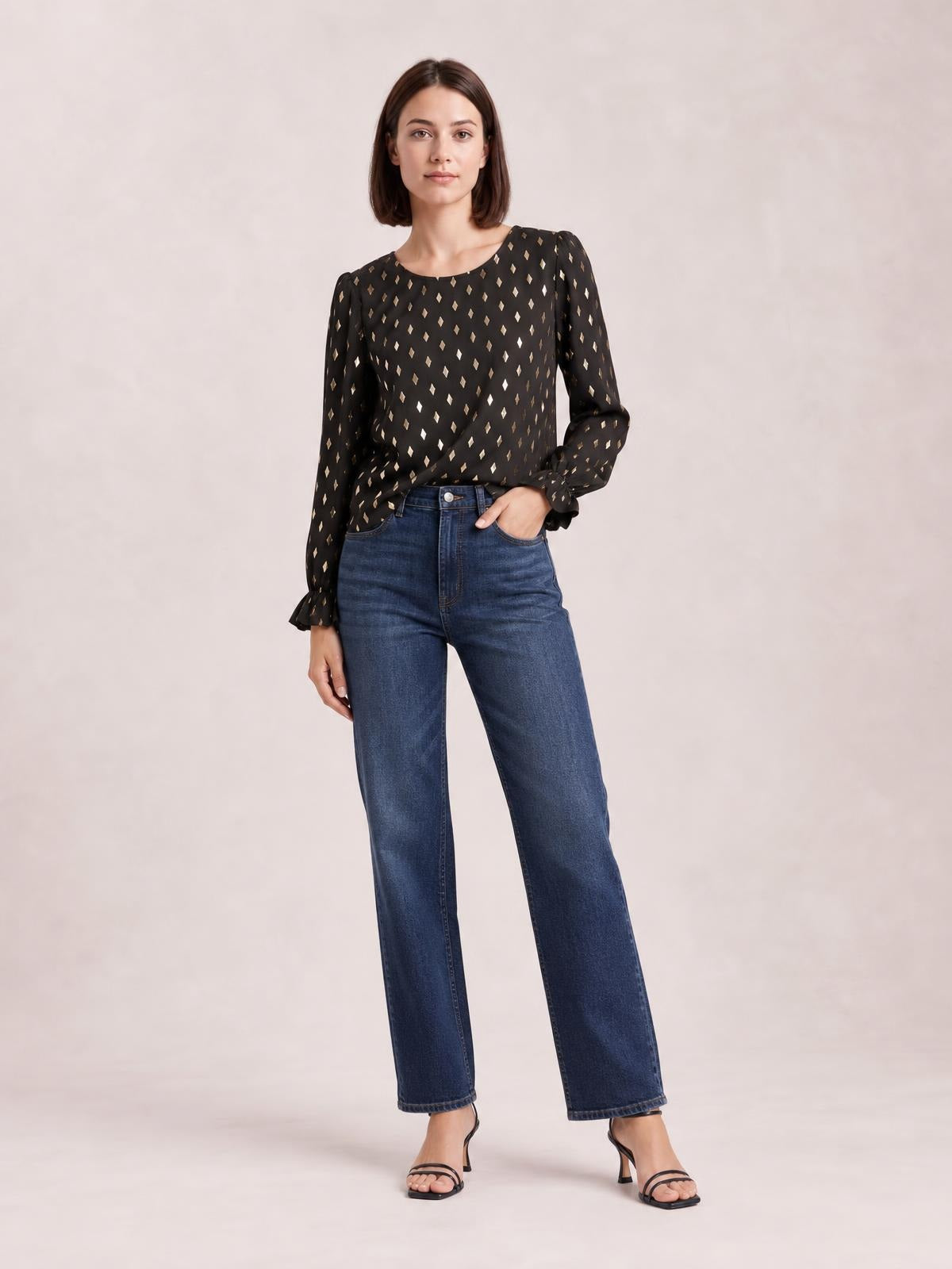 Model standing with one hand in her pocket wears a black printed blouse with a round neck, long puff sleeves, flounce cuffs, and a relaxed silhouette.