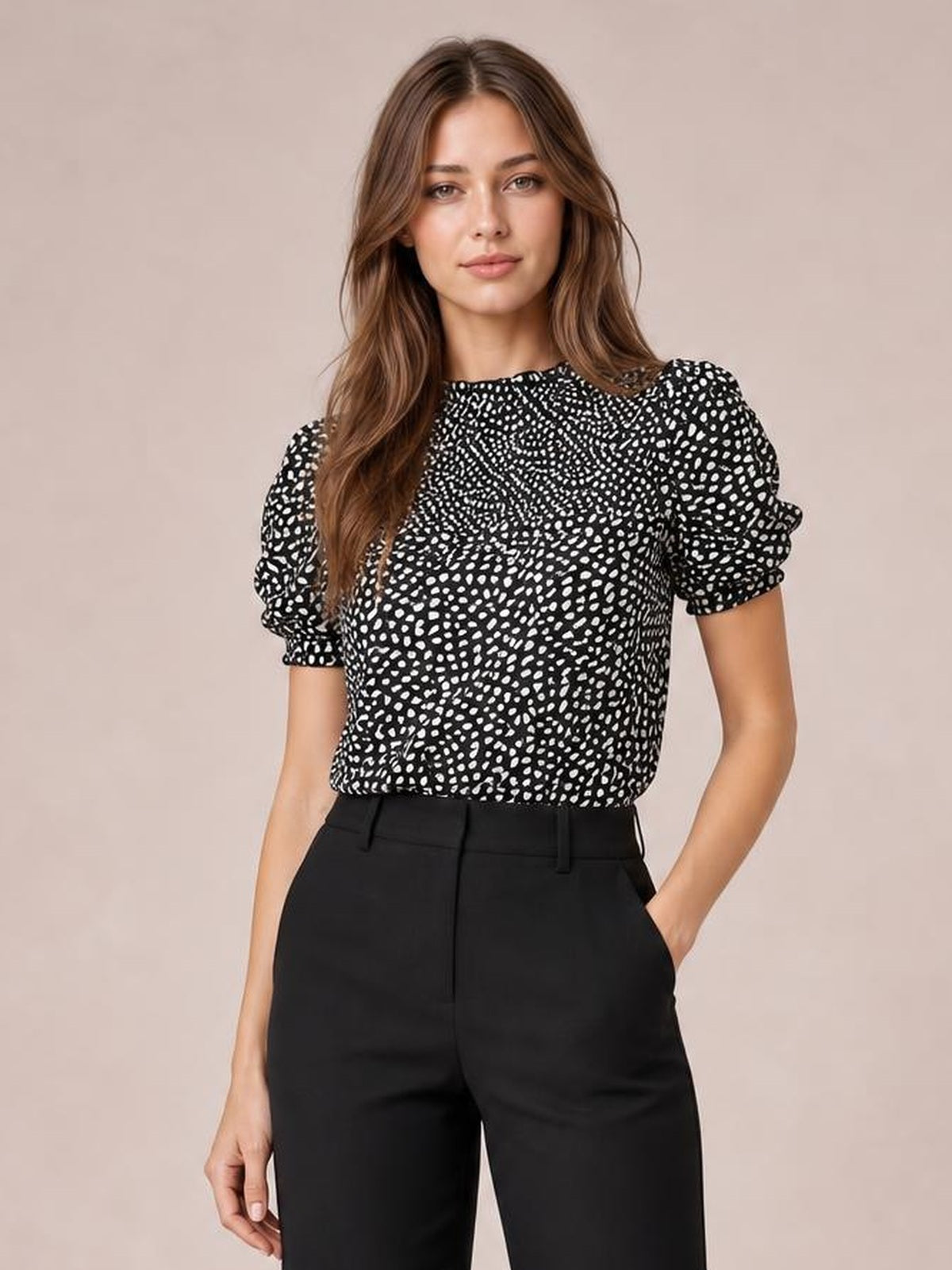 Model wearing a black printed round neck blouse with short puff sleeves, an opaque relaxed silhouette, and one hand in her trouser pocket.
