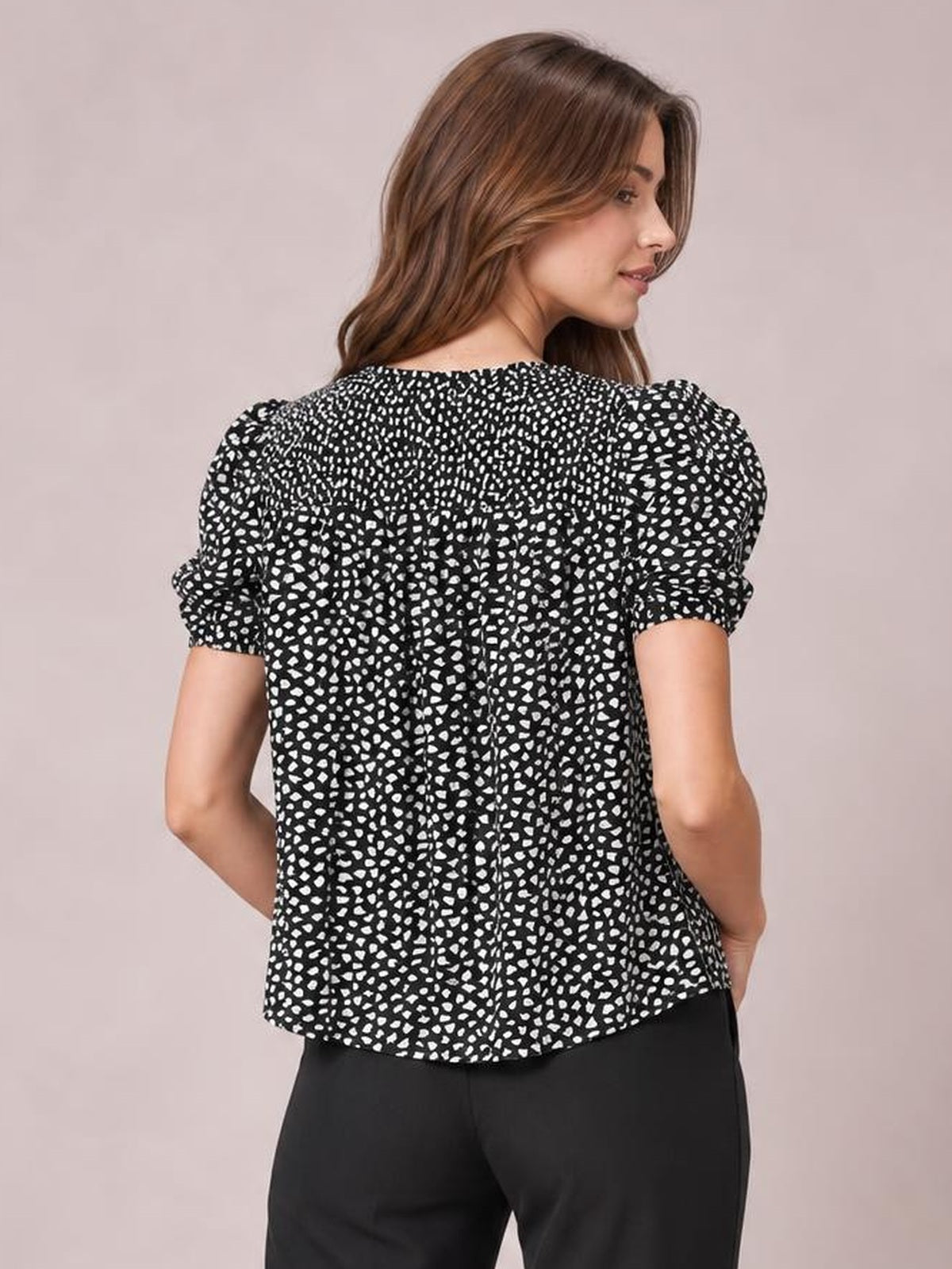 Model shown from the back in a black printed blouse with a round neck, short puff sleeves, and a relaxed long silhouette.
