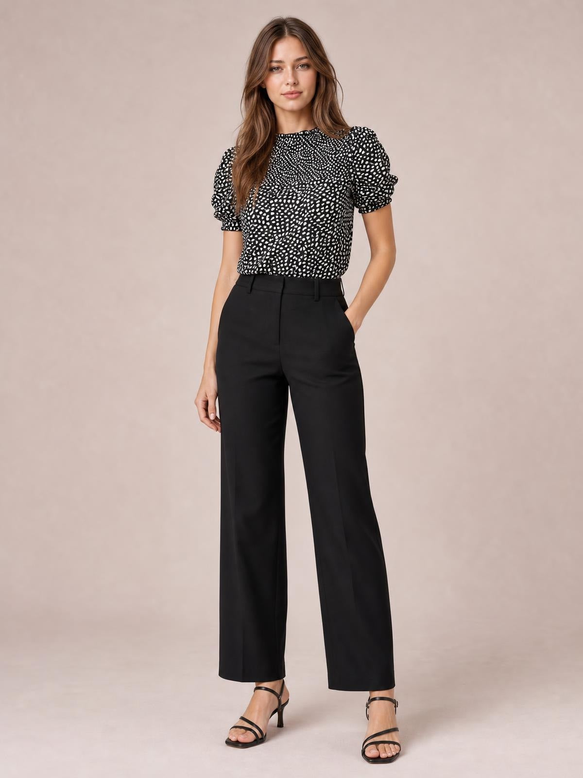 Model poses in a black-and-white printed round neck blouse with short puff sleeves and a relaxed long silhouette, paired with high-waisted black trousers.