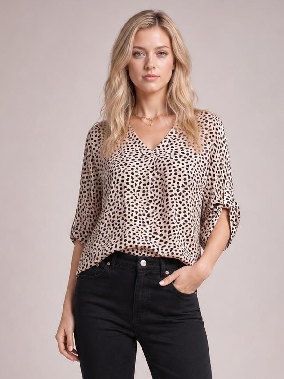 Model poses in a beige and black printed V-neck blouse with a relaxed silhouette and three-quarter roll-tab sleeves, paired with black jeans.