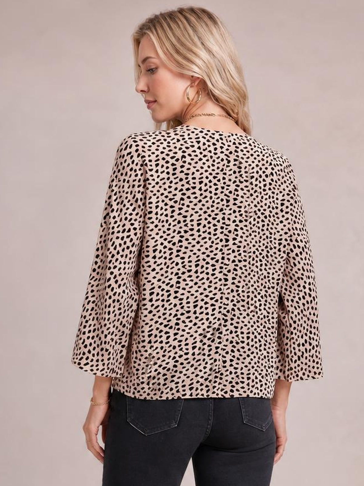 Model shown from the back wearing a beige printed blouse with black spots, a relaxed regular silhouette, and three-quarter sleeves ending just below the elbows.