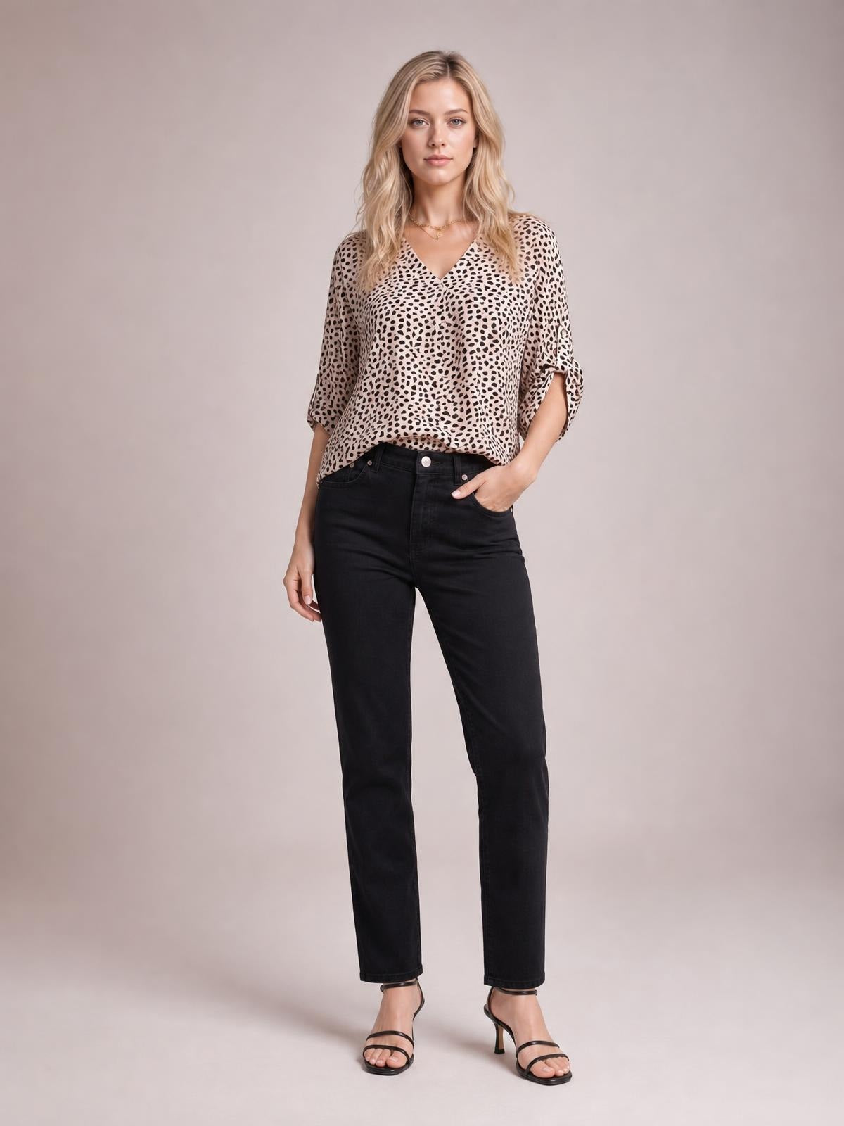 Model poses in a beige printed V-neck blouse with three-quarter roll-tab sleeves, a relaxed regular silhouette, and black jeans.