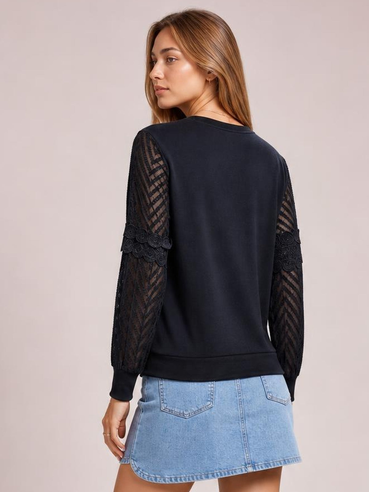 A model looks over her shoulder wearing a black round-neck blouse with a regular silhouette, long lace-patterned sleeves, and a straight hem.