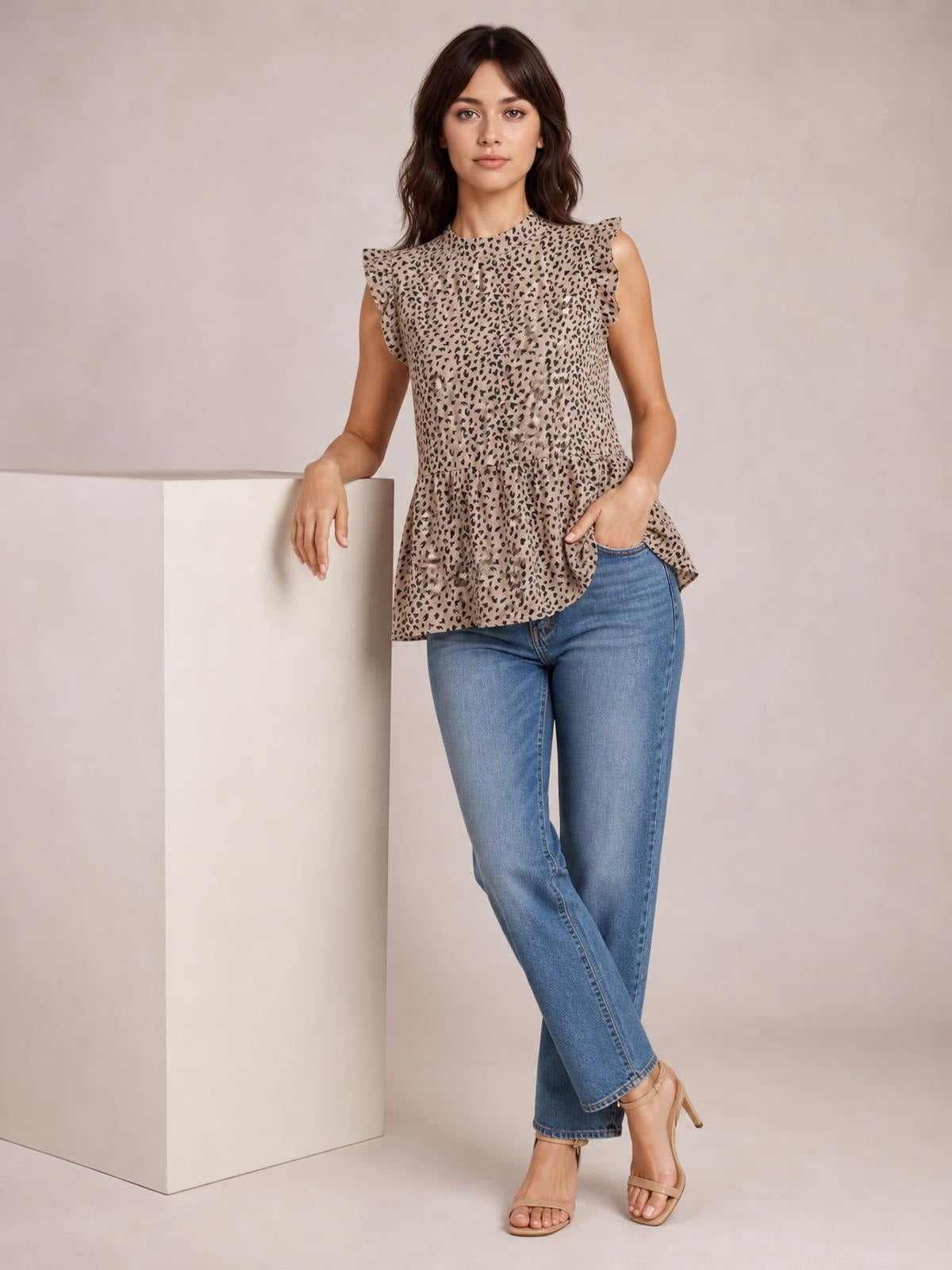 A model stands with crossed legs in a beige leopard-print blouse featuring a mock neck, buttoned front, ruffled cap sleeves, and a softly flared hem.
