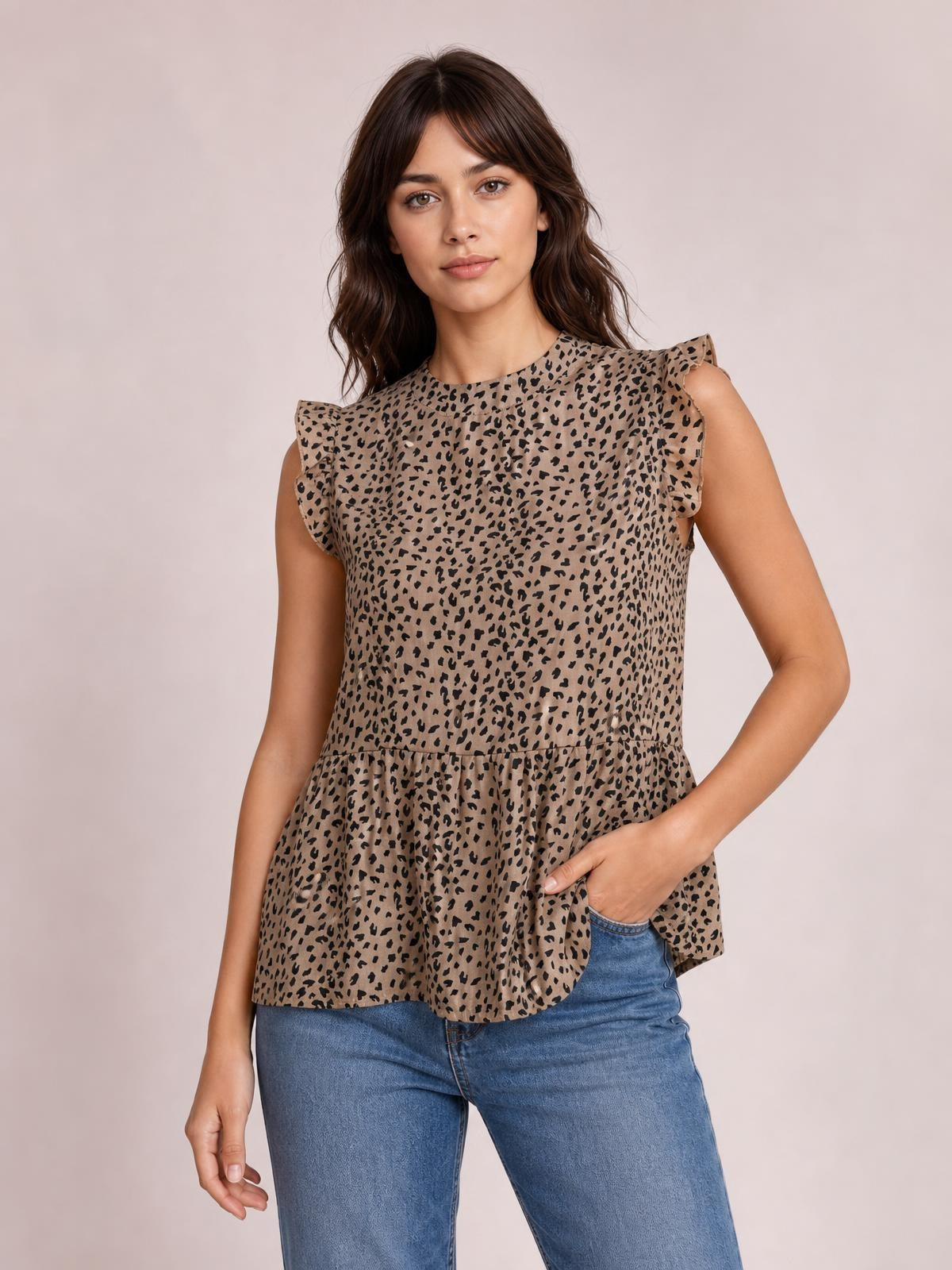 Model wearing a taupe leopard-print blouse with a mock neck, ruffled cap sleeves, and a loose peplum silhouette, posing with one hand in her jeans pocket.