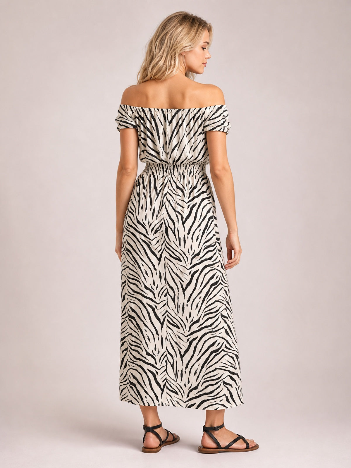 Model shown from behind in a white and black animal-print midi dress with an off-shoulder neckline, short sleeves, gathered waist, and flowing silhouette.