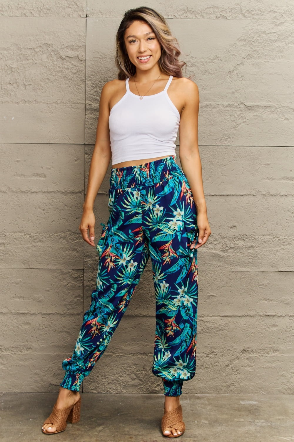 Model poses in colorful navy plant-print long pants with a smocked elastic waist, relaxed silhouette, and elastic cuffs.