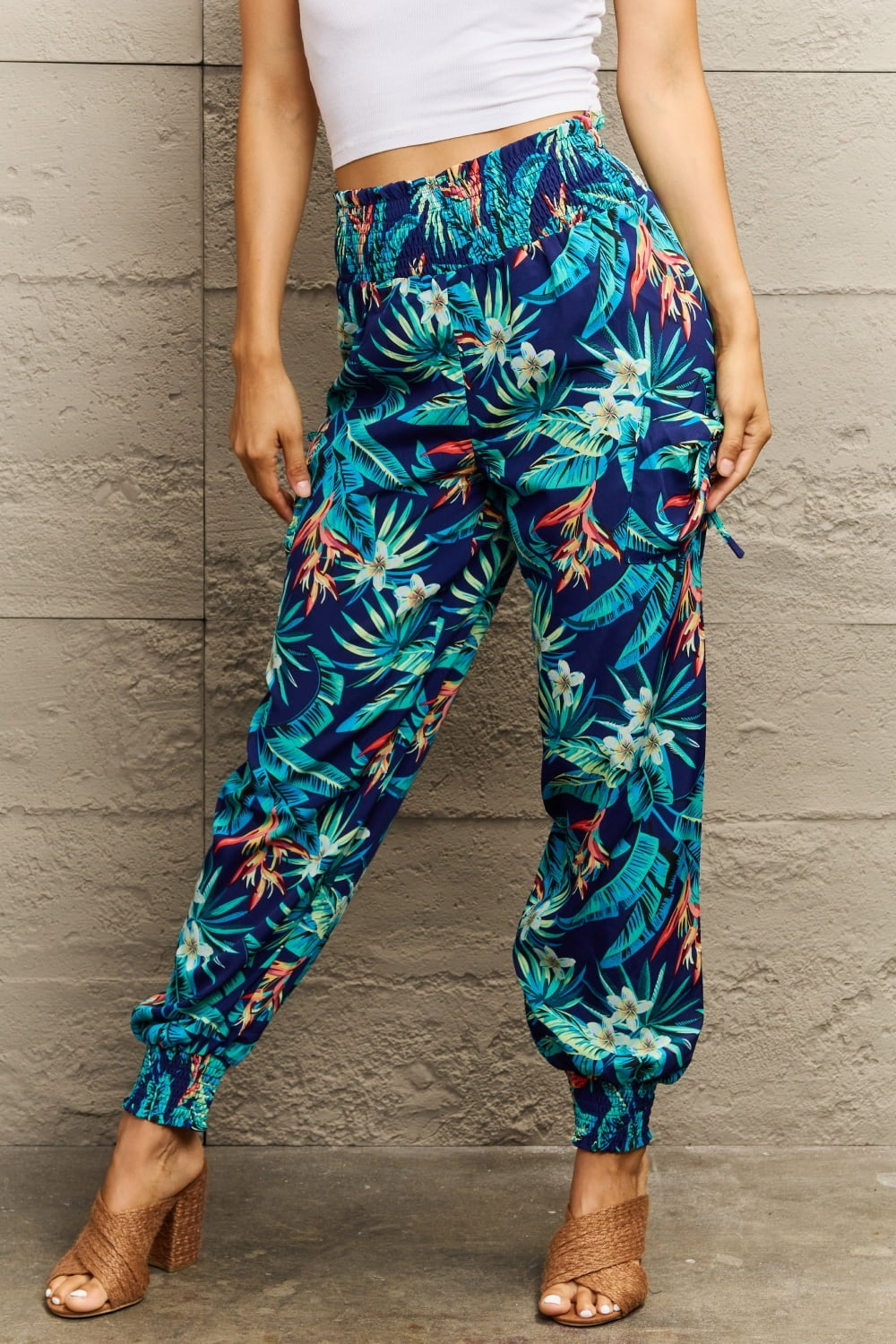 Model wearing navy smocked plant print long pants with a relaxed silhouette, elasticized waistband and ankle cuffs, standing with hands at the sides.