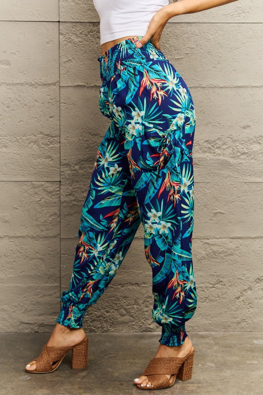 Model poses in navy blue smocked plant print long pants with a relaxed silhouette, elasticized waistband and gathered ankle cuffs.