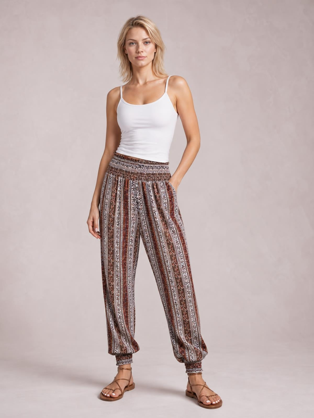 Model poses in brown and white printed high-waist pants with a smocked waistband, relaxed leg, side pockets, and elasticized ankle cuffs.