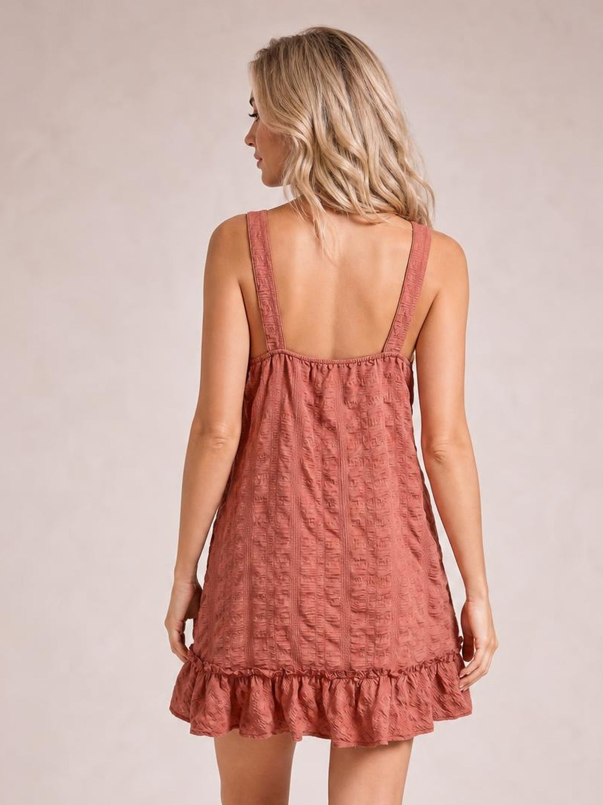 Model shown from the back in a textured rose mini dress with wide straps, a relaxed A-line silhouette, and a gathered ruffled hem.
