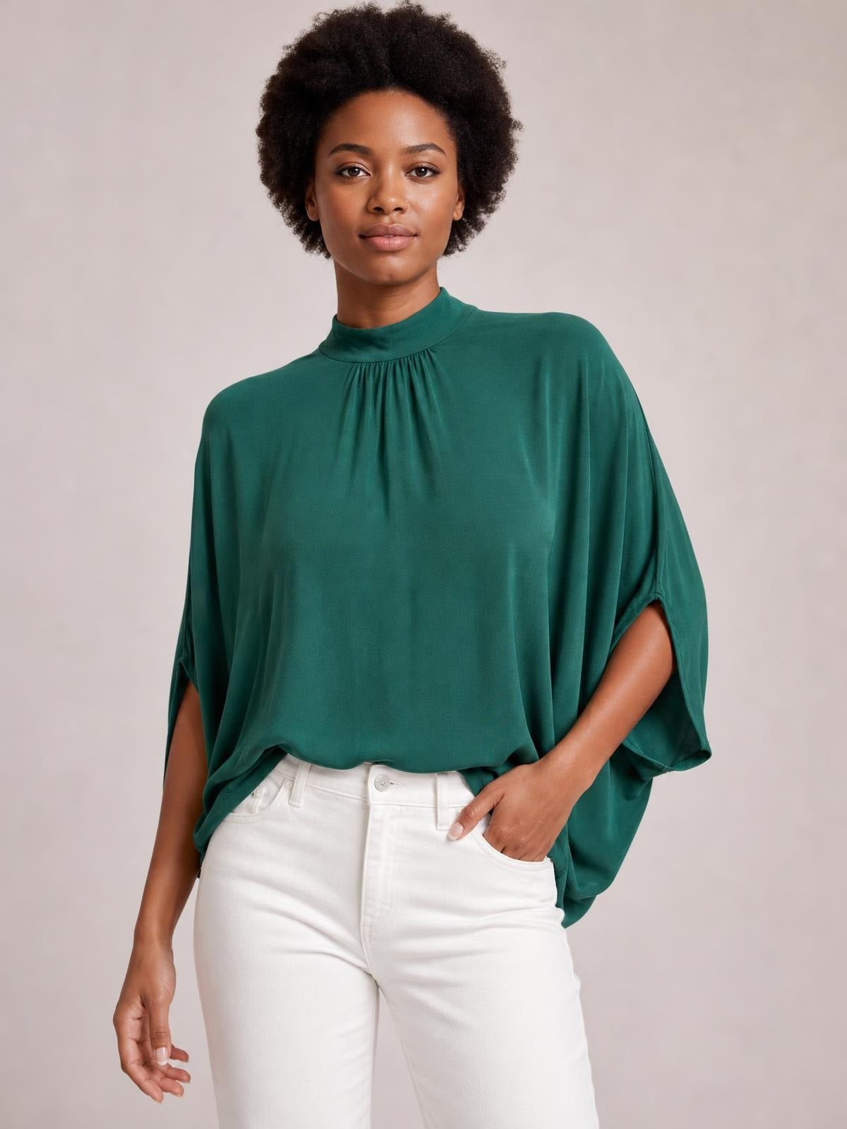 Model stands in a teal tie back mock neck blouse with ruched neckline, split three-quarter sleeves, and a relaxed, flowing silhouette.