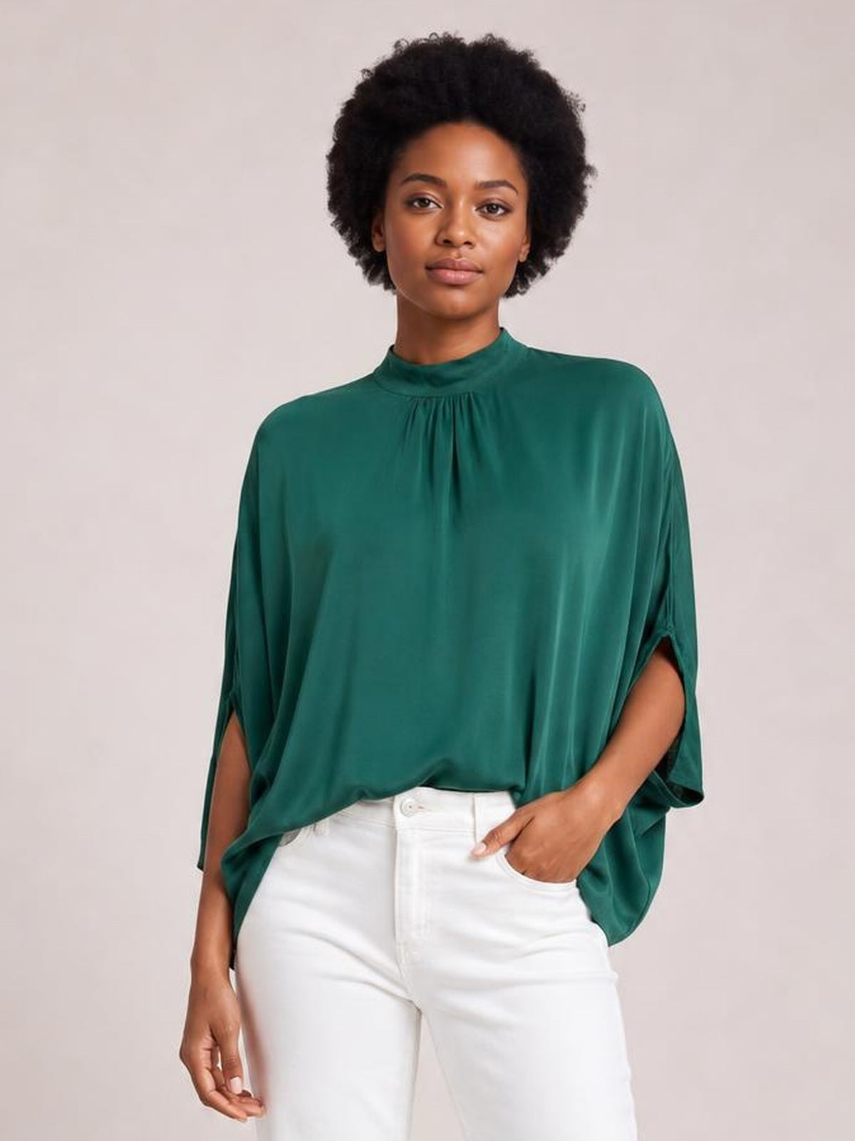 A model wears a solid teal mock neck blouse with ruched detailing, a relaxed draped silhouette, and three-quarter split sleeves with her hand in a pocket.