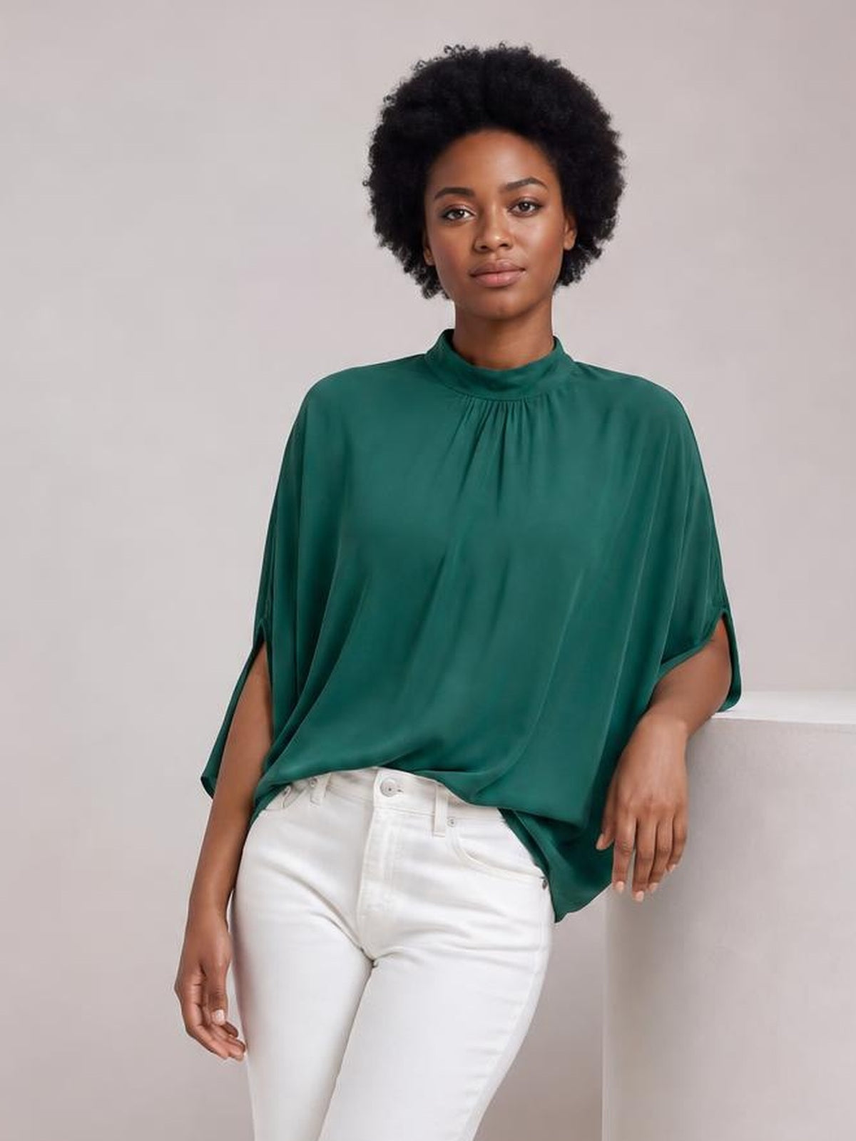 A model wears a solid emerald green blouse with a ruched mock neck, split three-quarter sleeves, and a relaxed draped silhouette.