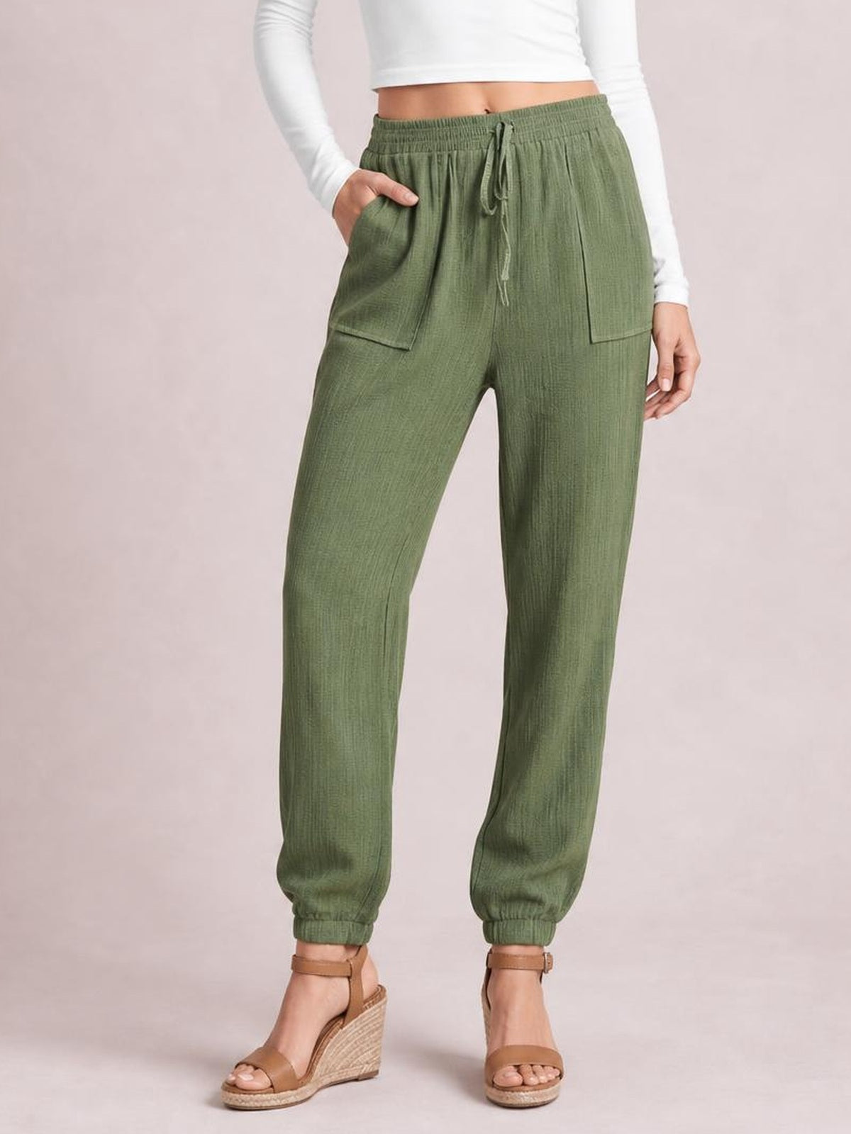 Model wearing solid olive-green tie waist long pants with an elastic waistband, drawstring, side pockets, relaxed tapered legs, and gathered cuffs.
