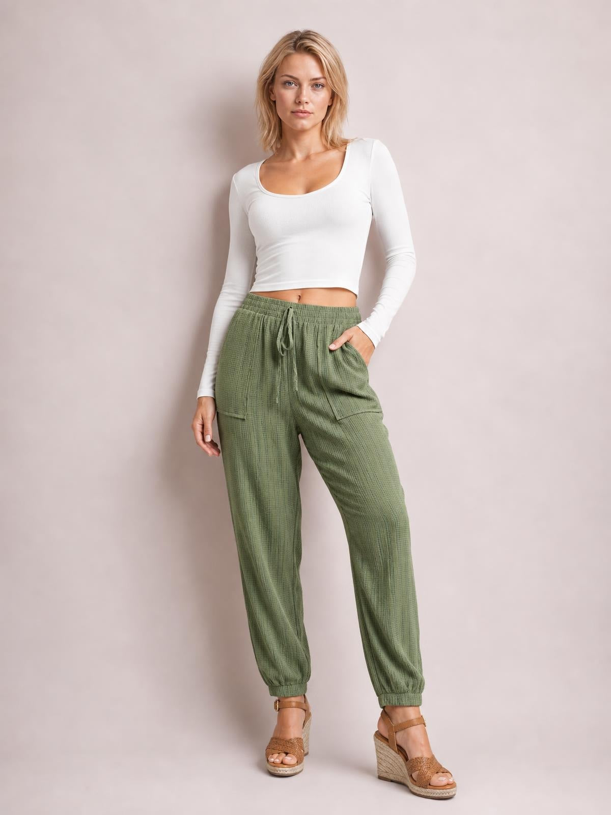 Model wearing solid olive-green tie waist long pants with a relaxed tapered silhouette, drawstring waistband, side pockets, and elastic cuffs.
