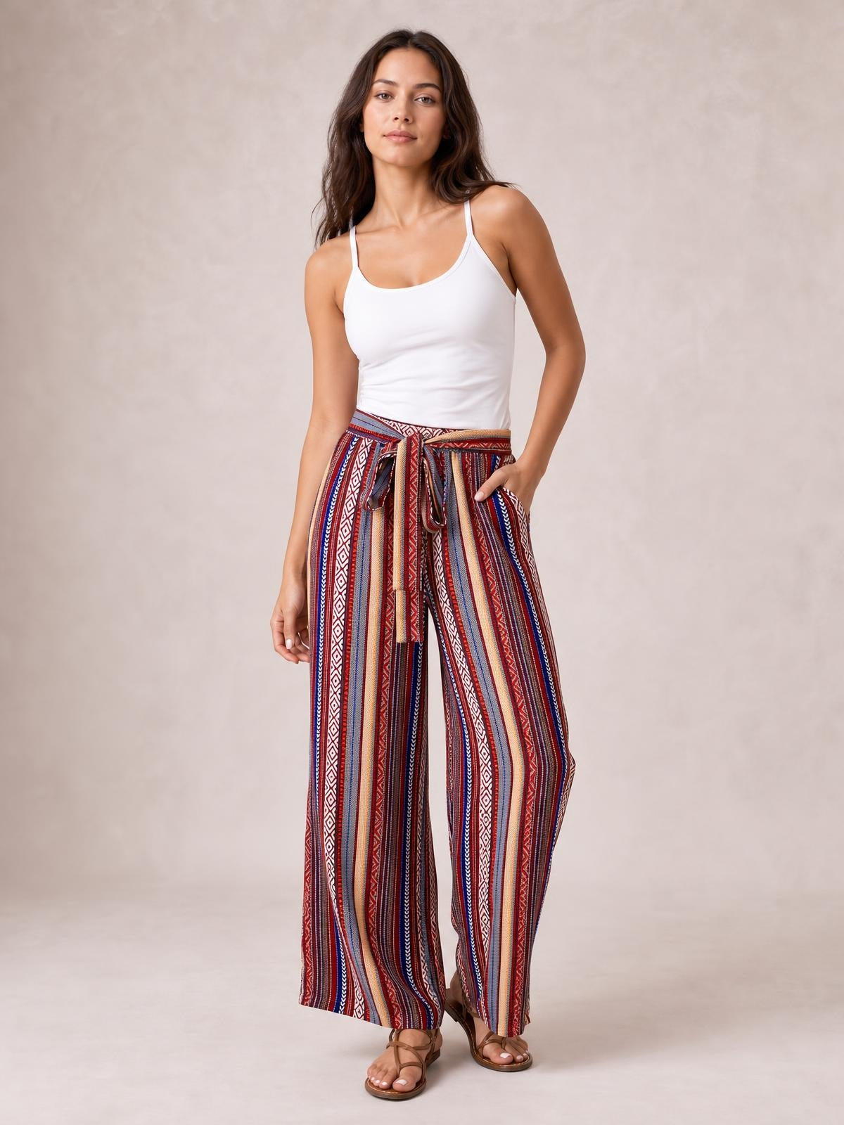 Model stands in multicolored geometric wide-leg pants with vertical stripes, a tied waist, flowy silhouette, and visible side pockets.