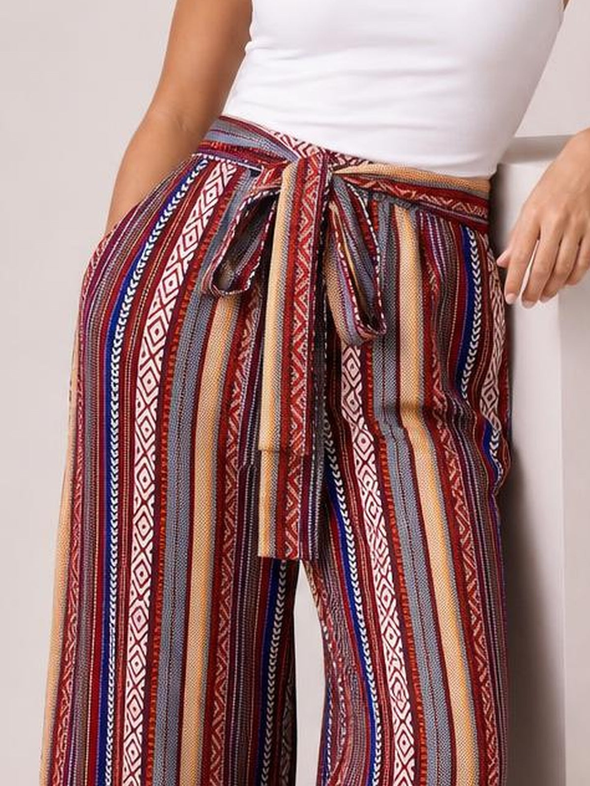 Model wears multicolored geometric wide-leg pants with vertical stripes, a tied waist, and visible pockets, styled with a fitted white top.