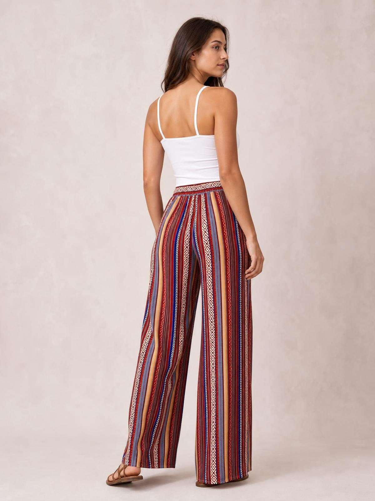 Model poses in multicolored geometric-print tied wide-leg pants with a high waistband and flowing full-length silhouette, shown from the back.