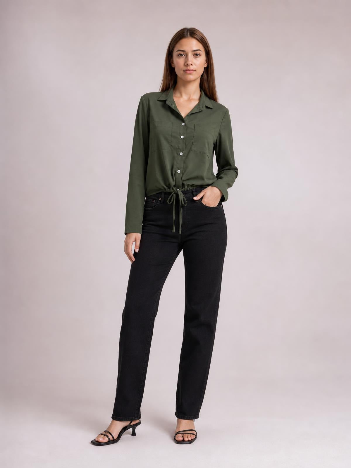 A model poses in an olive green long-sleeve button-down shirt with a collared neckline, front buttons, and a tied hem creating a relaxed silhouette.