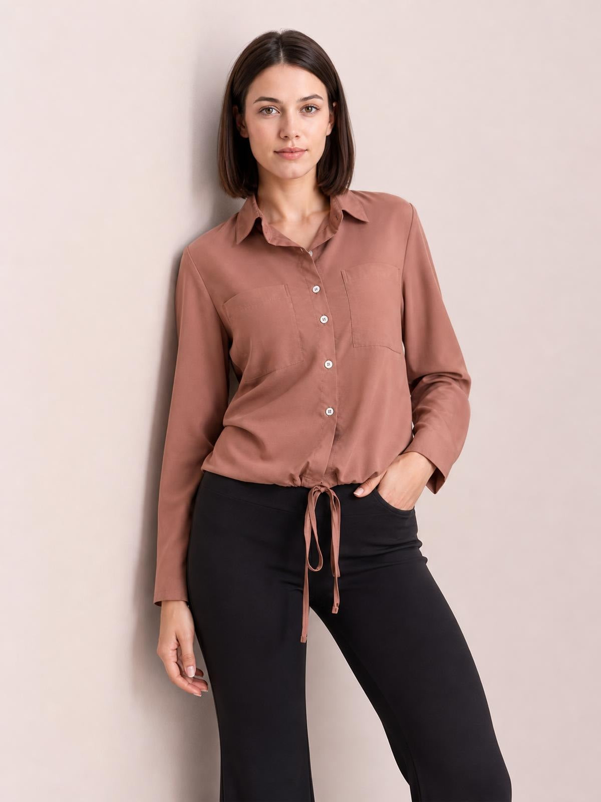A model stands in a rose-brown button-down long-sleeve shirt with a pointed collar, chest pockets, and a tied hem creating a softly gathered silhouette.