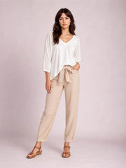 A model poses in beige tied high-waist pants with a relaxed straight-leg silhouette, visible side pockets, and cuffed hems.