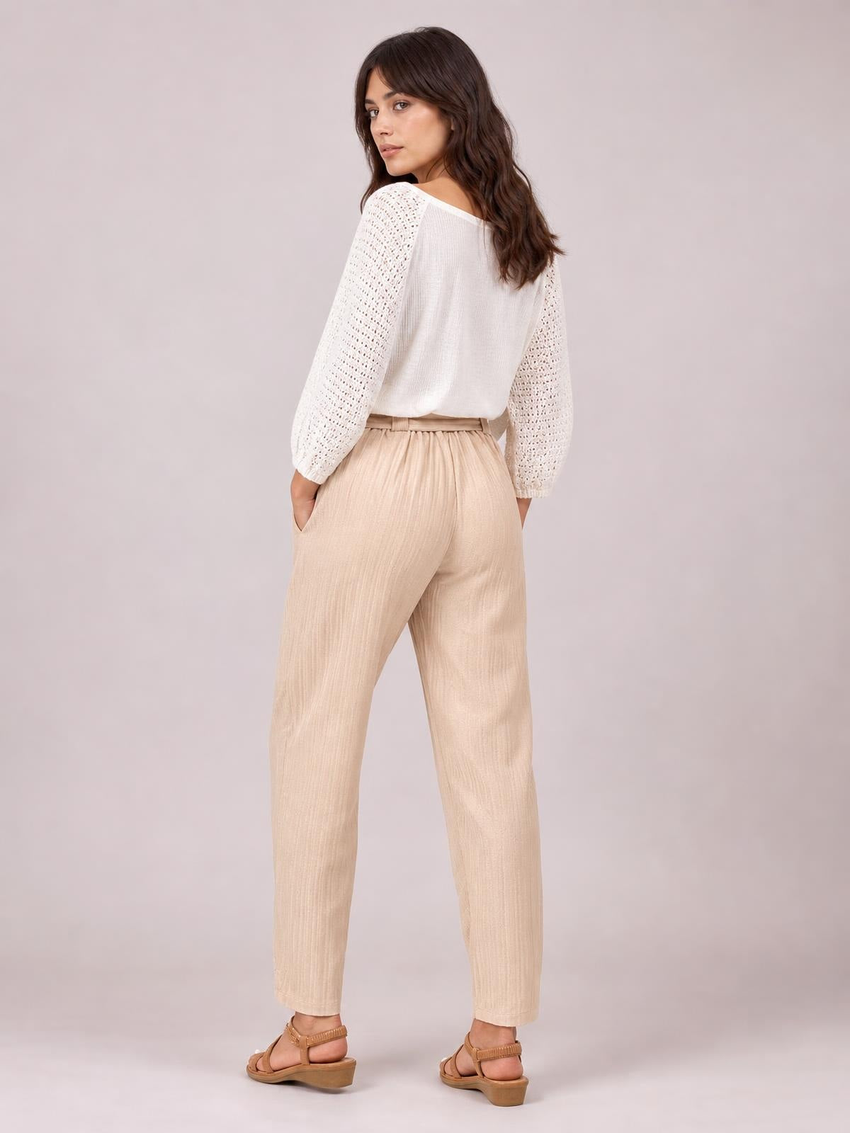 A model poses from behind in beige tied high waist pants with a relaxed straight-leg silhouette and visible side pockets.