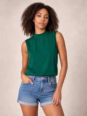 A model wears a solid emerald green sleeveless blouse with a mock neck, gathered neckline, and relaxed regular silhouette, posing with one hand in her pocket.
